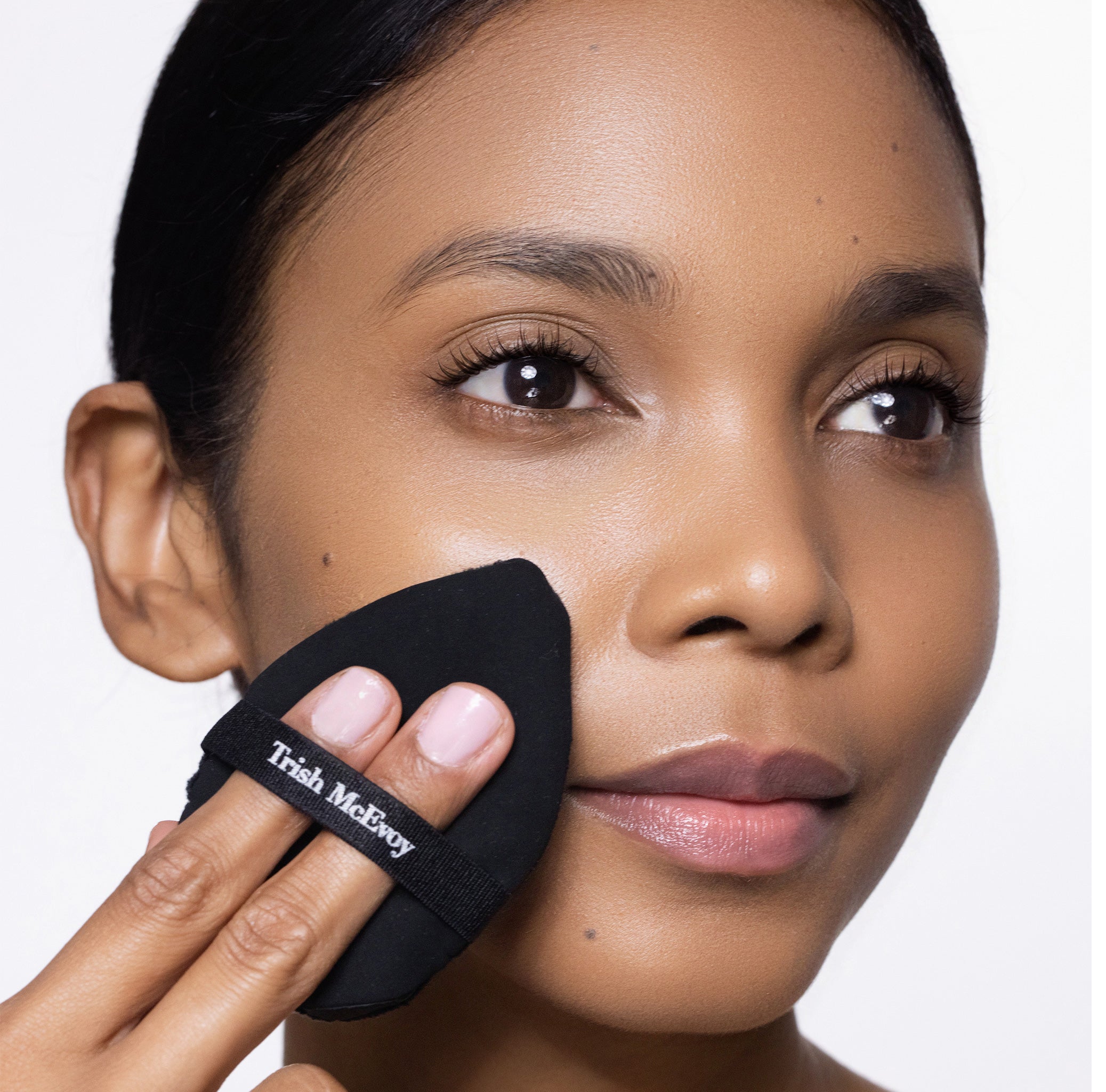 Woman using a Trish McEvoy makeup sponge applicator on her face.