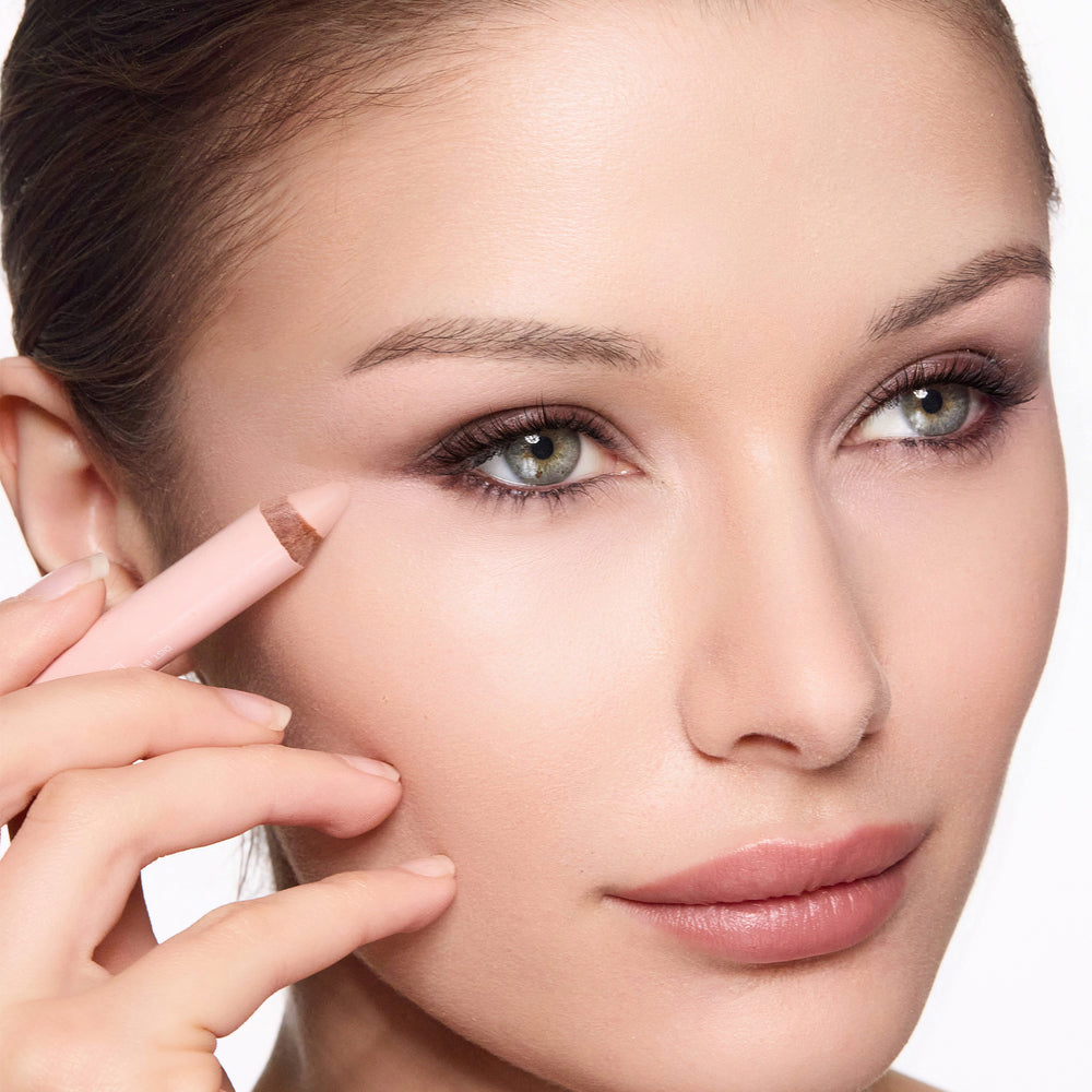 Close-up of a woman applying eye brightening pencil to her face.