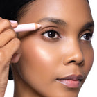 Woman applying makeup with eye brightening pencil near her eye on a white background