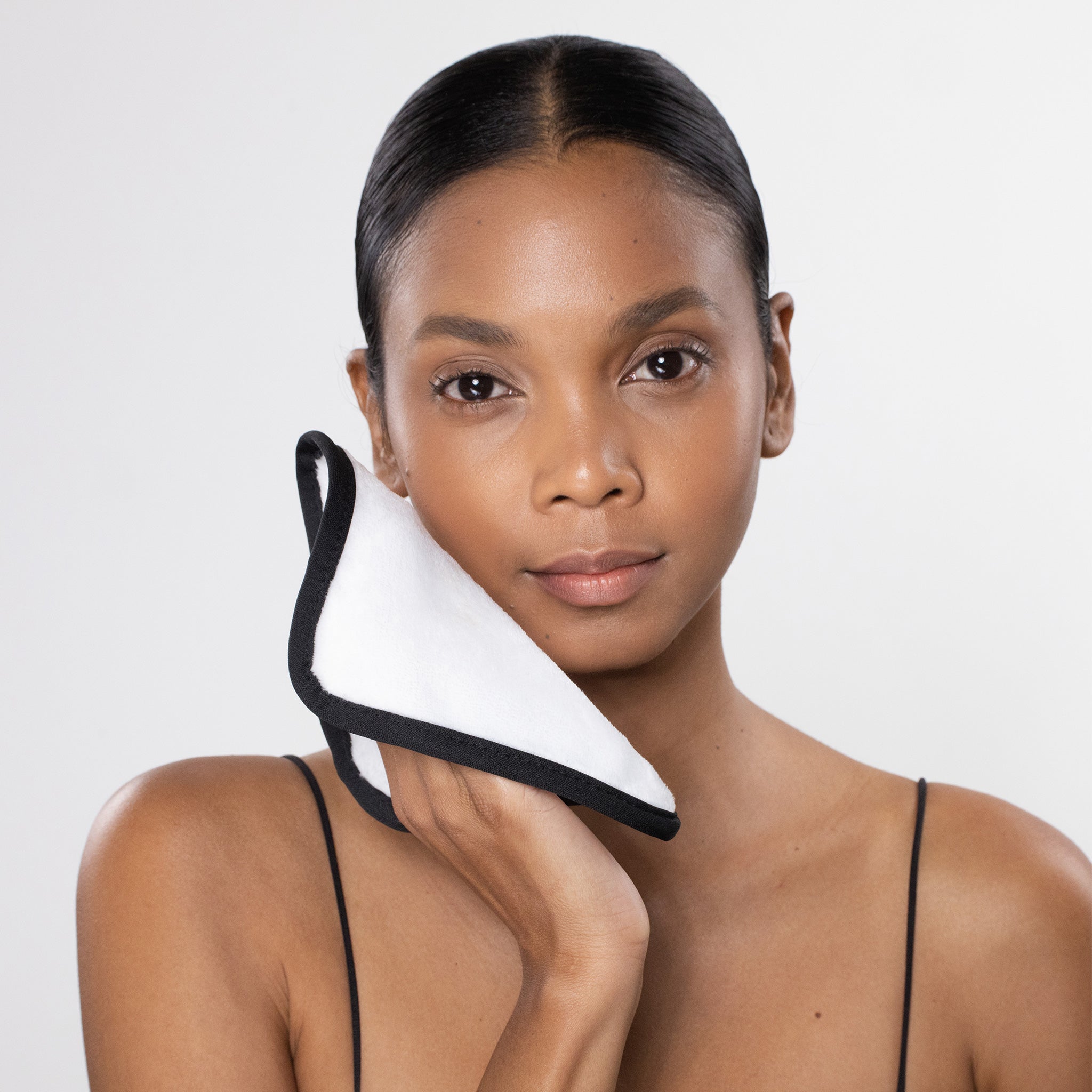 Woman holding a black and white product against her neck on a plain background