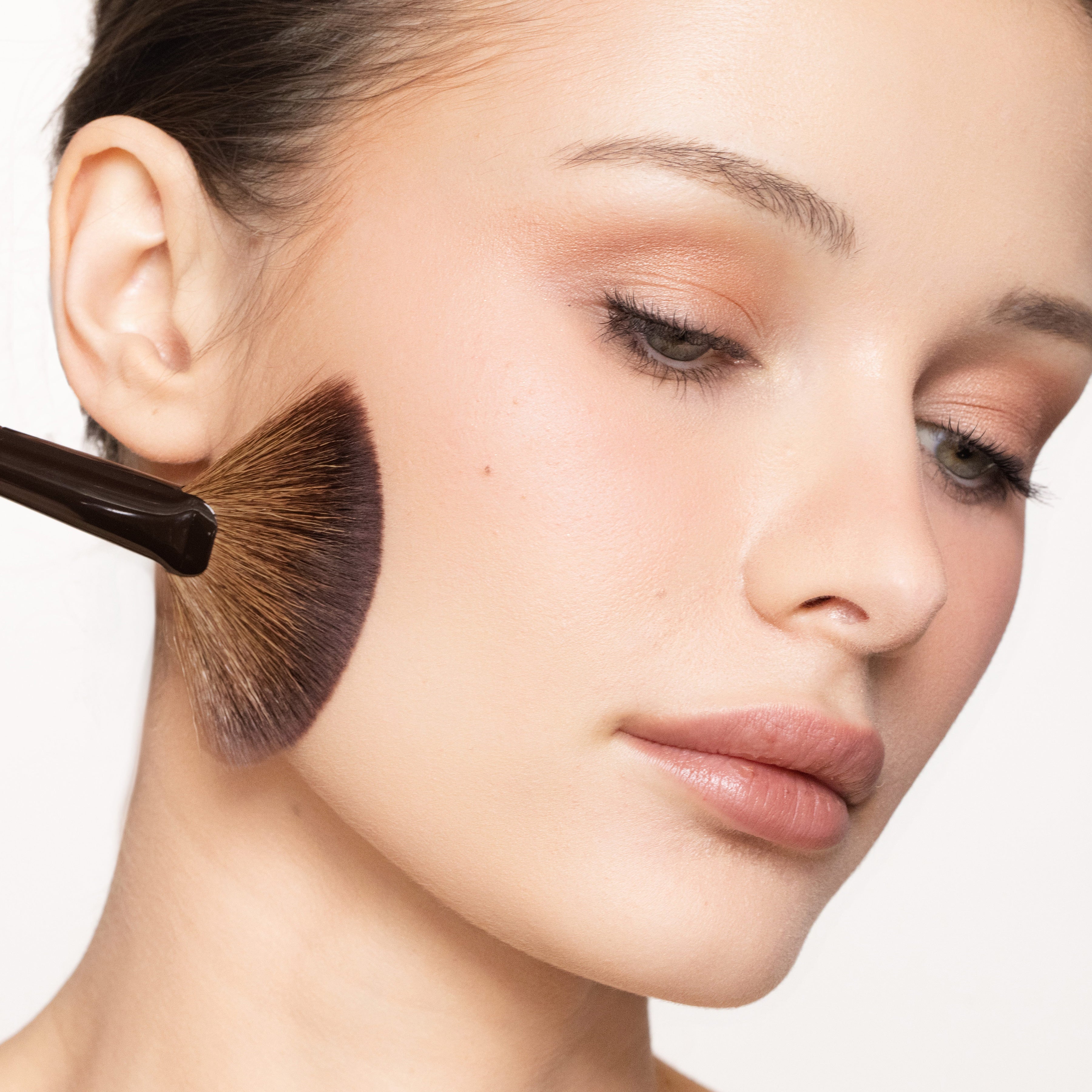 Woman having makeup applied with a brush on a white background