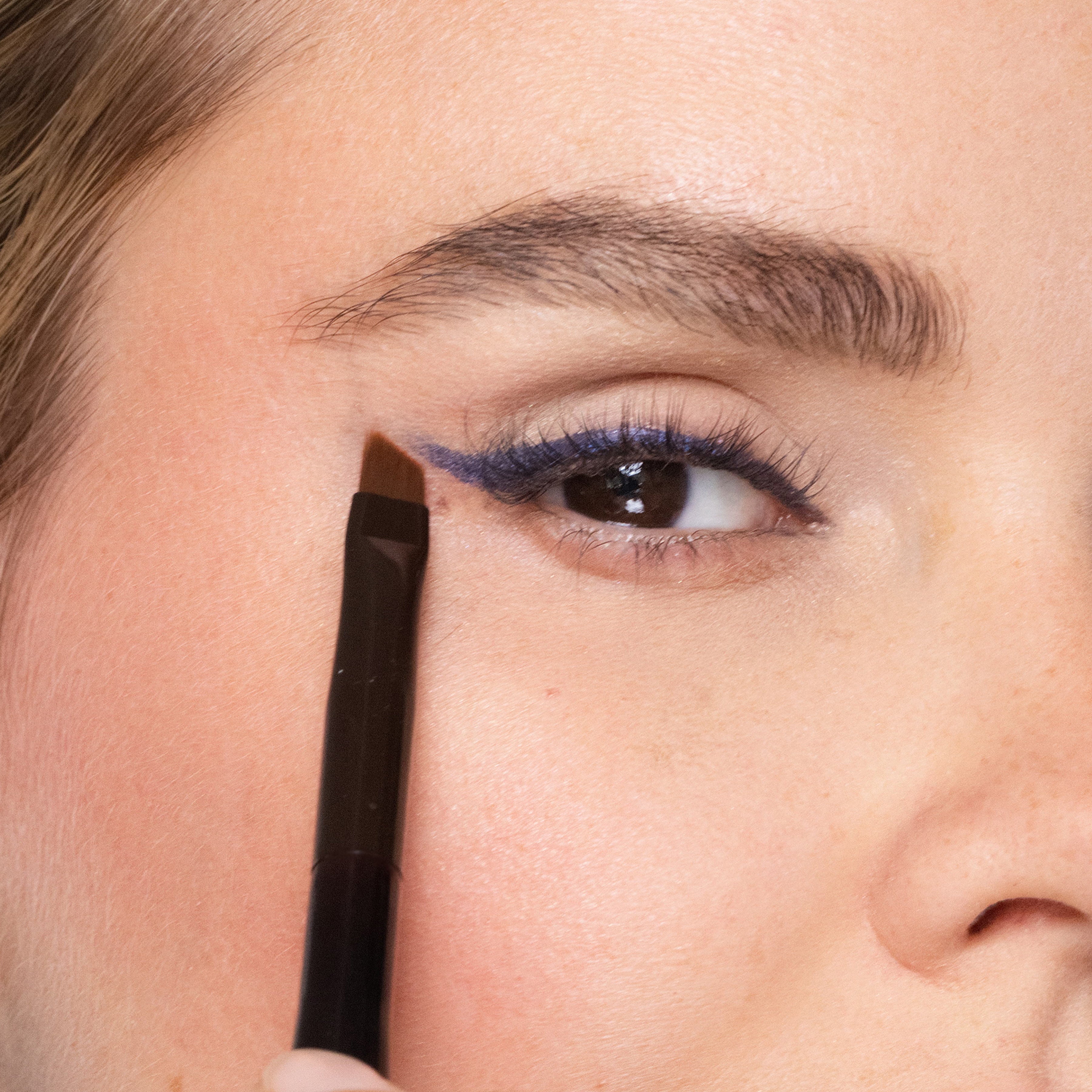 Close-up of a person applying eyeliner with a brush.