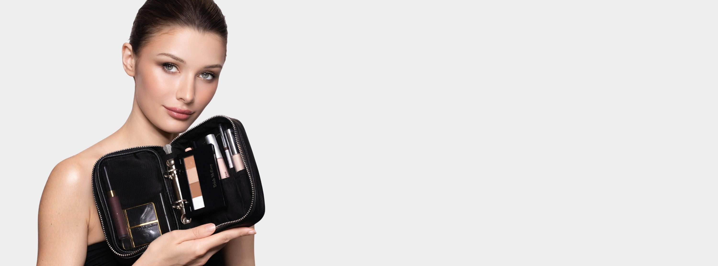 Woman holding a black makeup case with cosmetic products on a light gray background