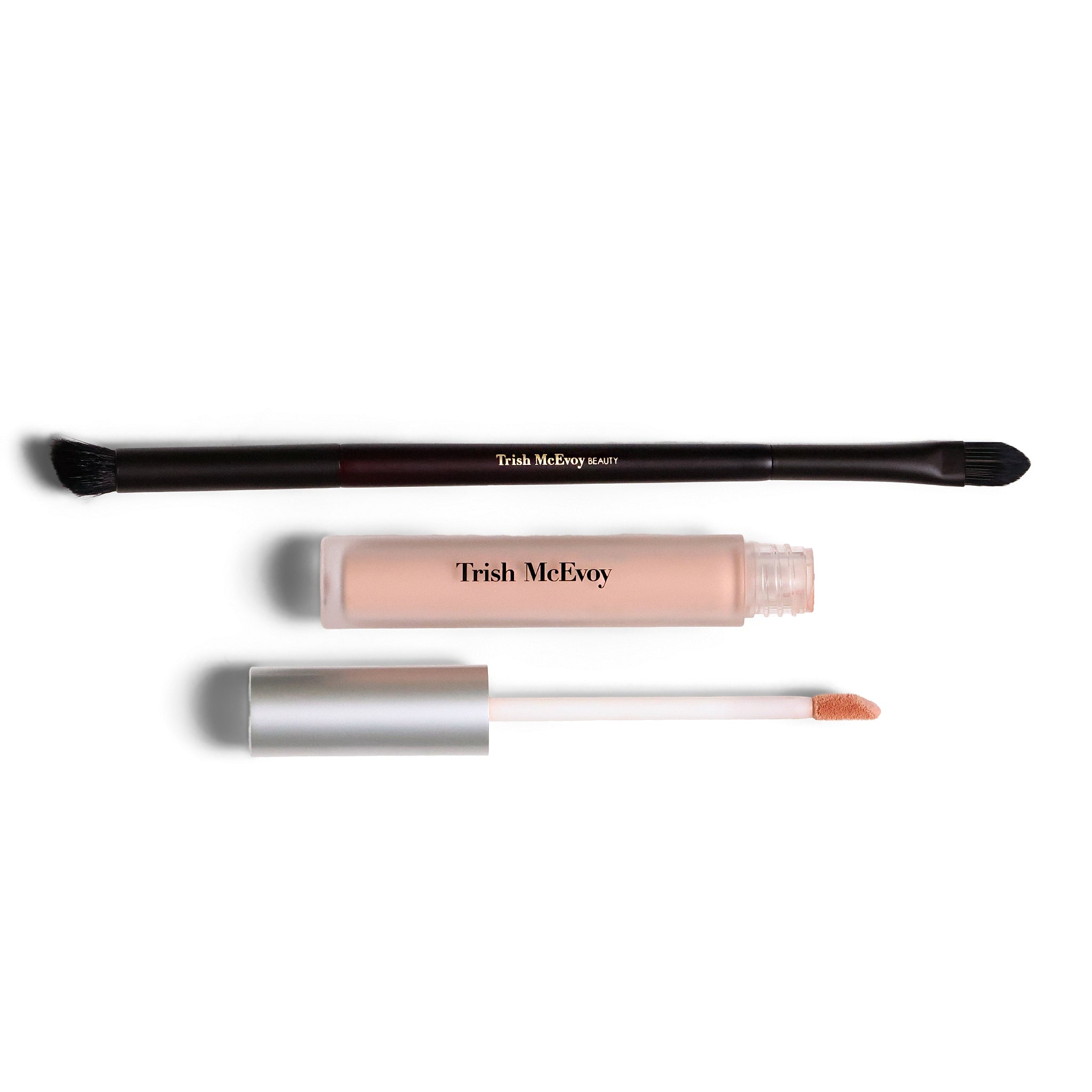 Trish McEvoy makeup set featuring a dual-ended applicator brush, a clear tube of liquid product in a nude pink shade, and its silver cap and doe-foot applicator wand, all displayed on a clean white background.