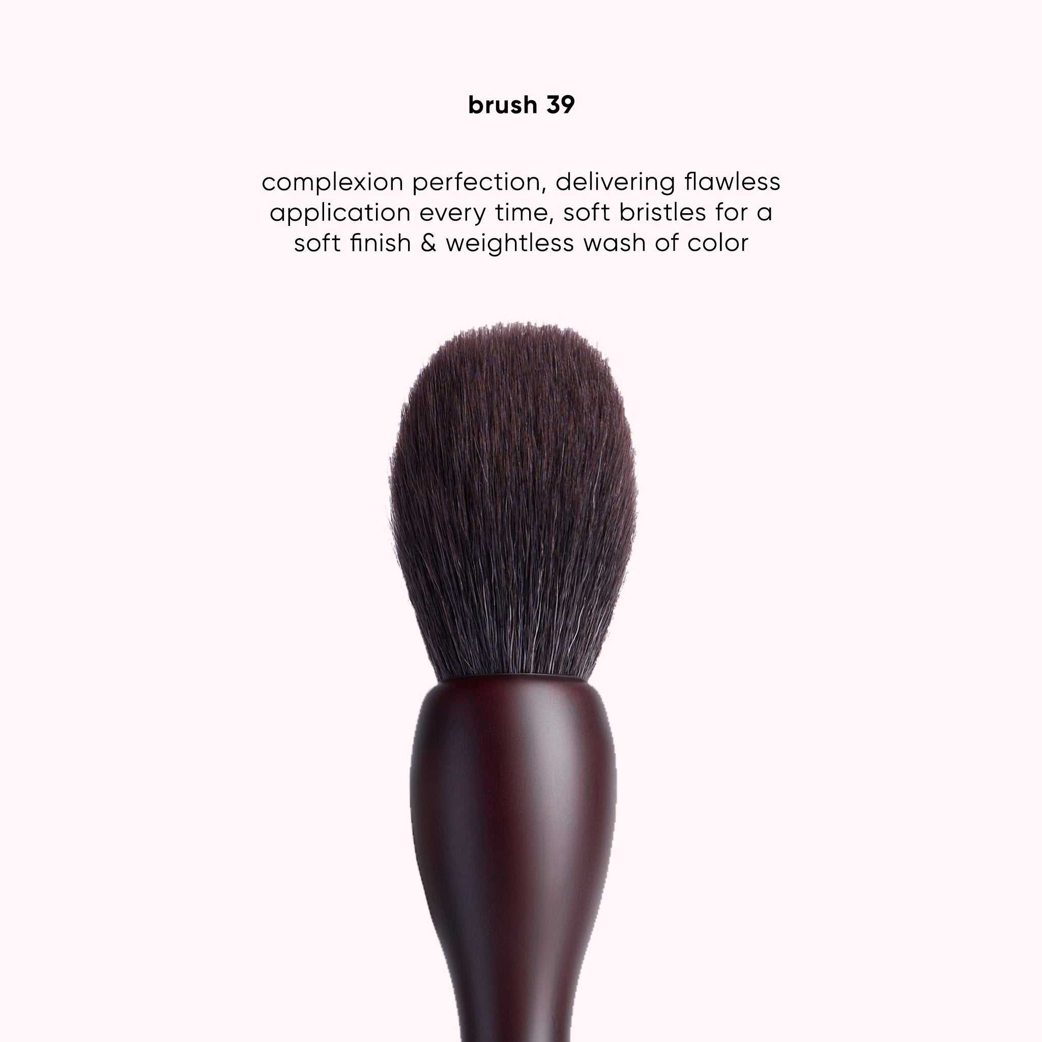 A makeup brush with dark brown bristles and a dark brown wooden handle, centered on a very pale pink background with descriptive text above.