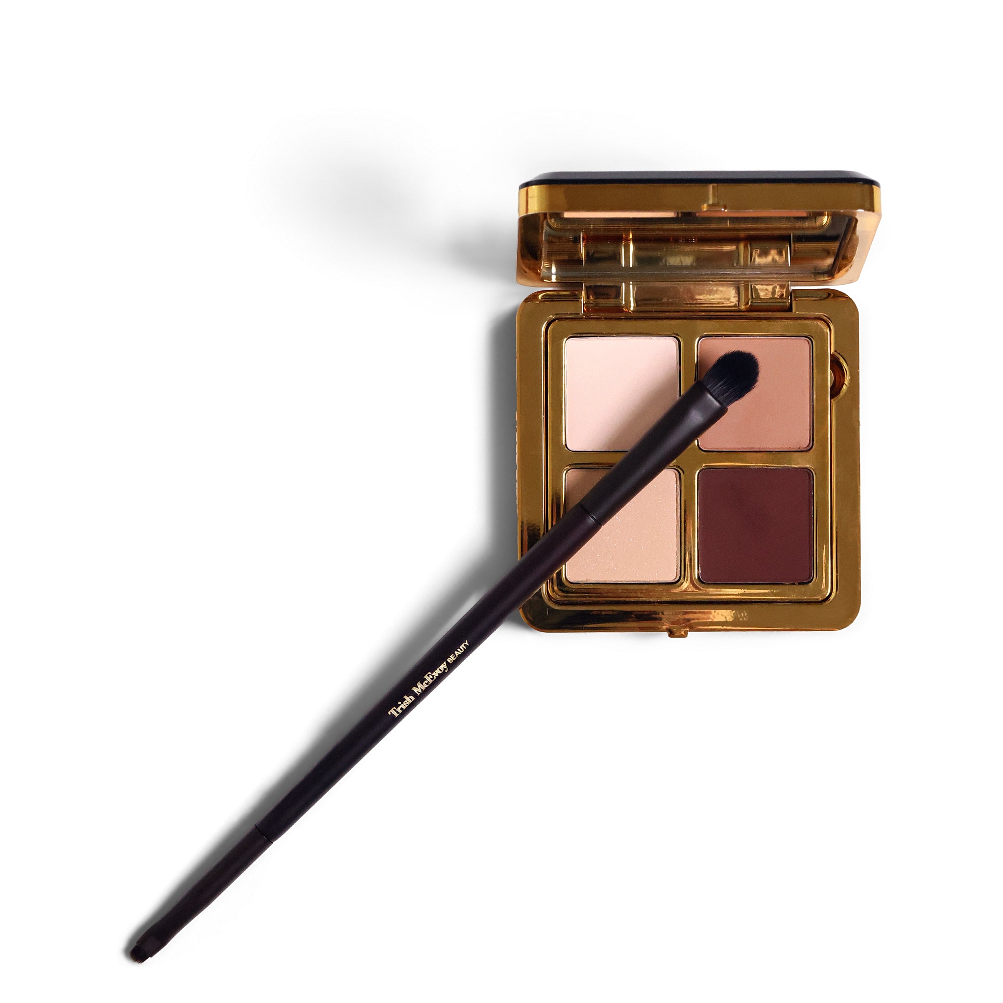 A four-shade eyeshadow palette in a gold compact with a black applicator brush resting across it, photographed on a clean white background.