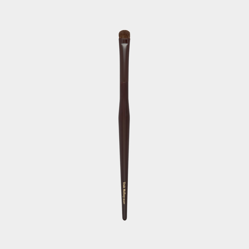Makeup brush with brown handle and black bristles on a light gray background