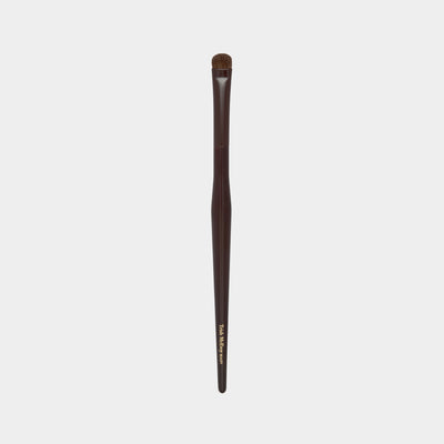 Makeup brush with brown handle and black bristles on a light gray background