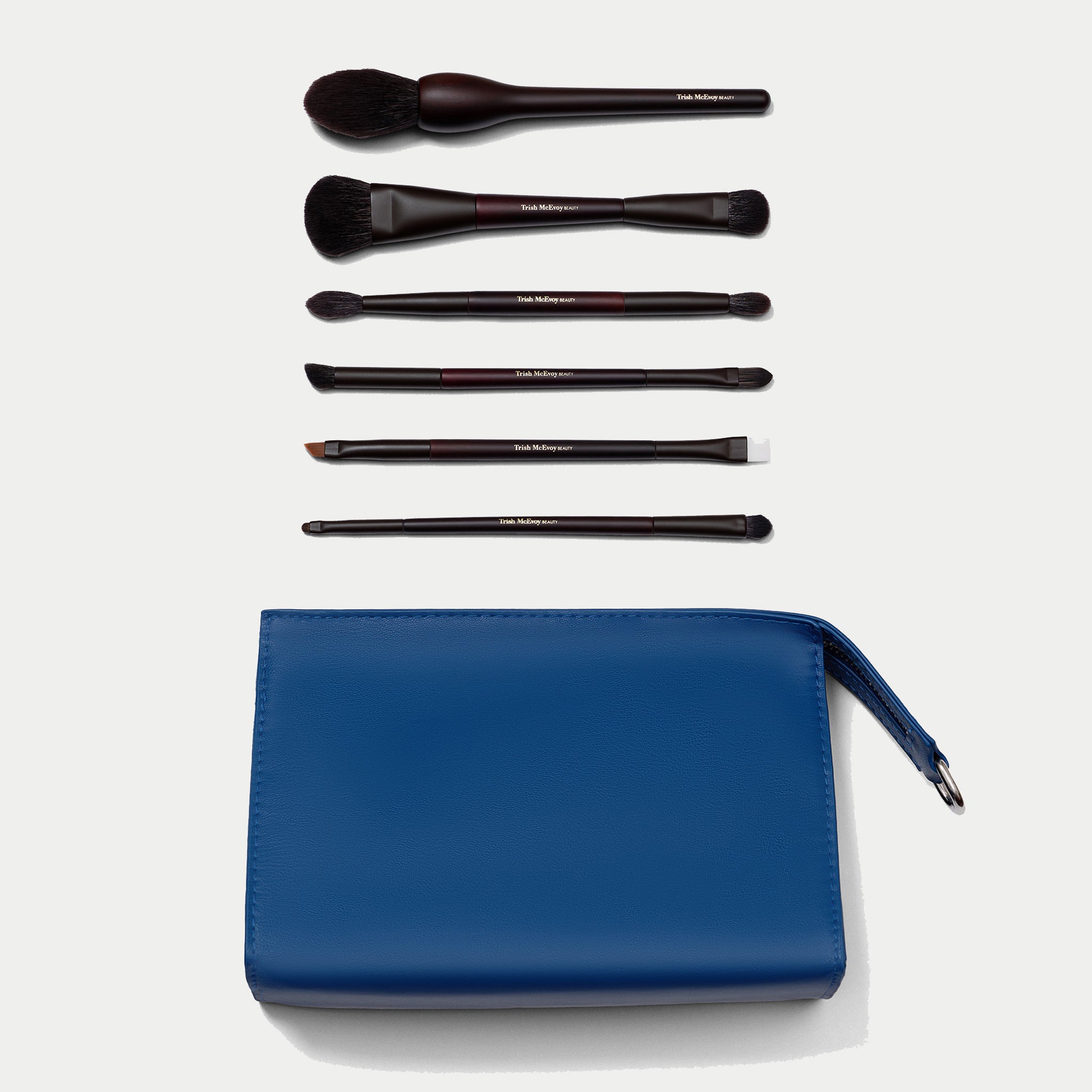A makeup brush set with six dark brown and black brushes arranged above a blue zip pouch on a light gray background.