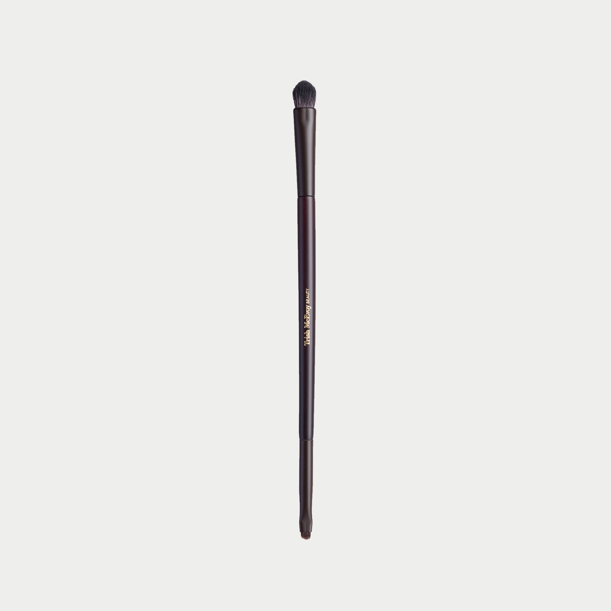 A single makeup brush with a dark brown handle and black bristles, featuring gold text that reads 'The Makeup Club' on a light gray background.