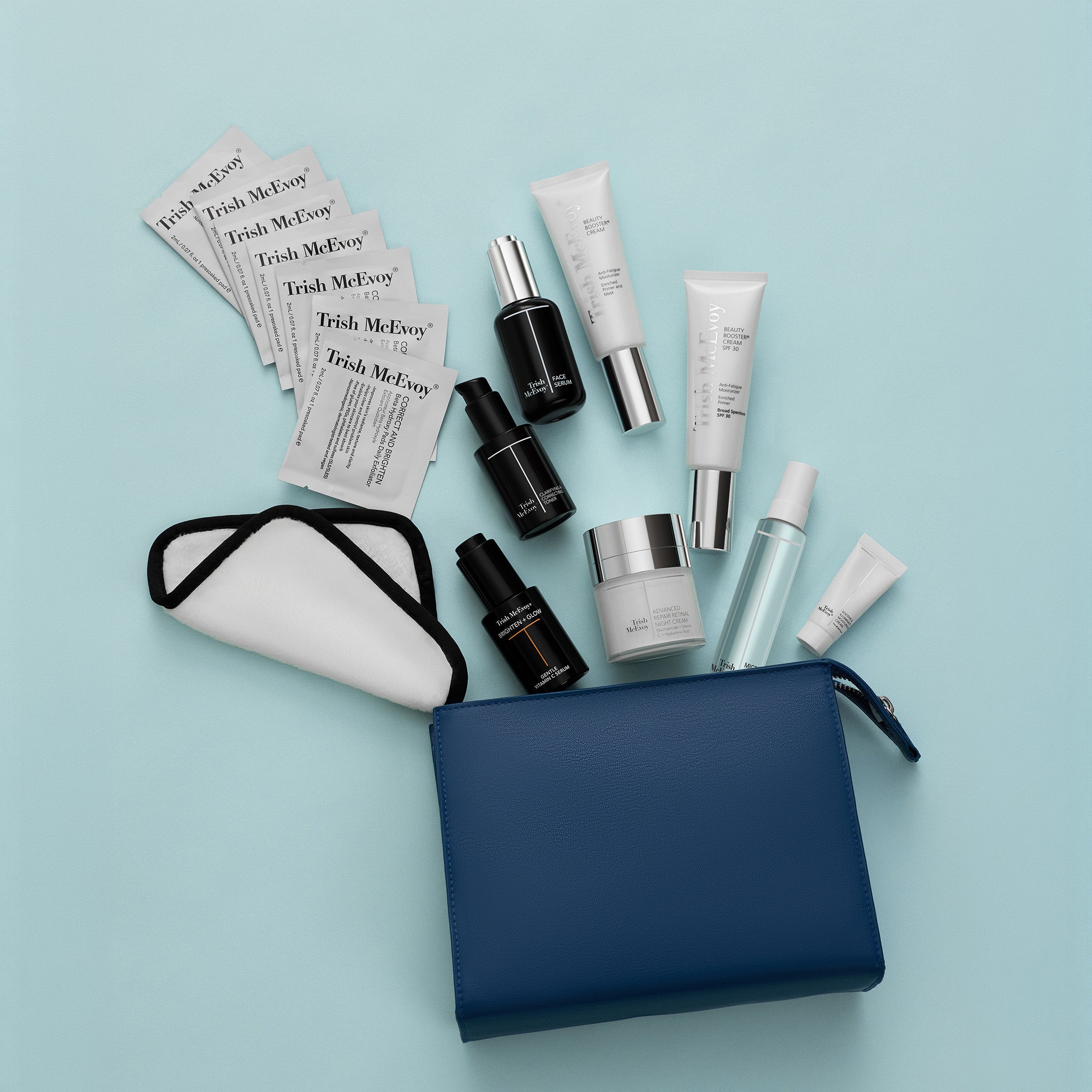 A flat-lay arrangement of skincare products and accessories on a light blue background, including multiple Fresh McEwen ampoules and tubes, a white cotton pad with black trim, and a navy blue zip pouch.