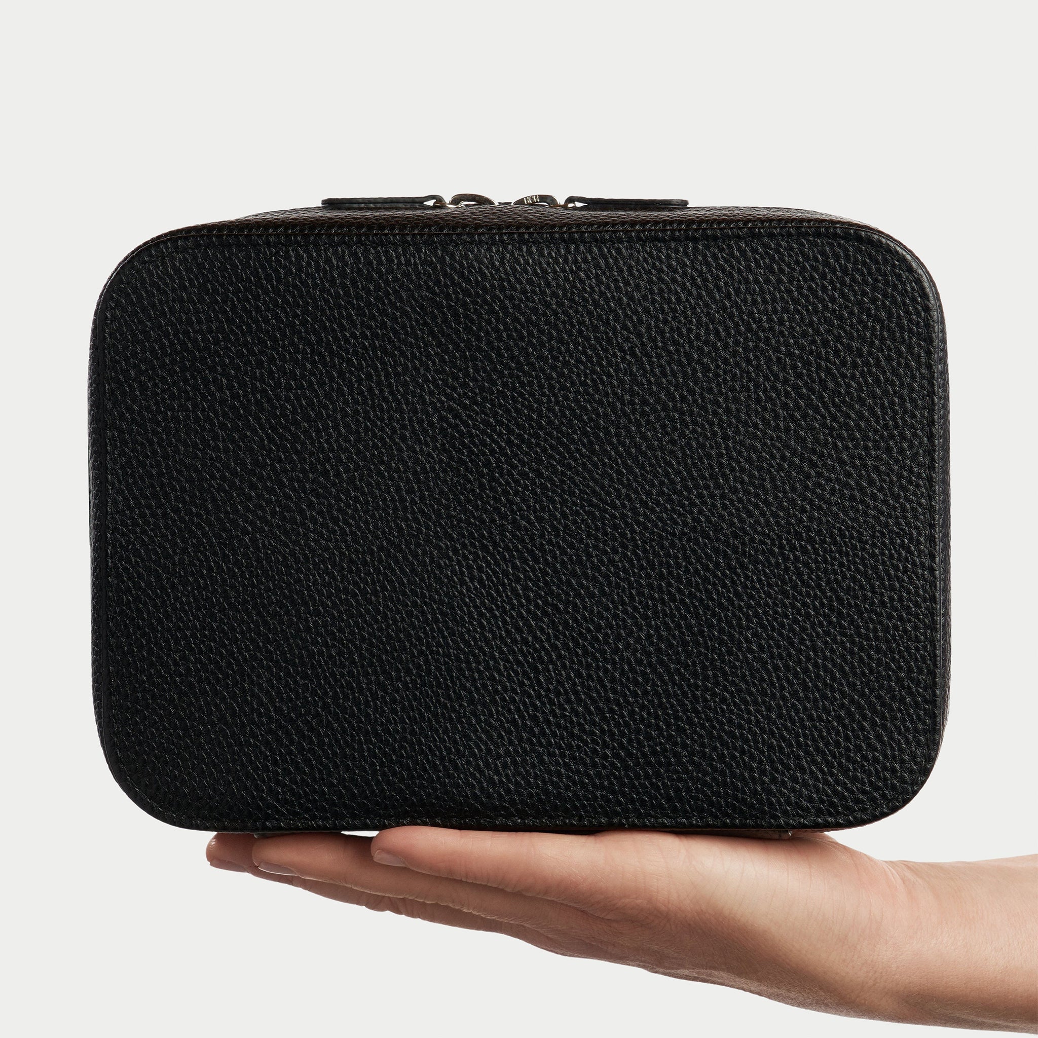 Black textured rectangular pouch held in a hand against a light gray background