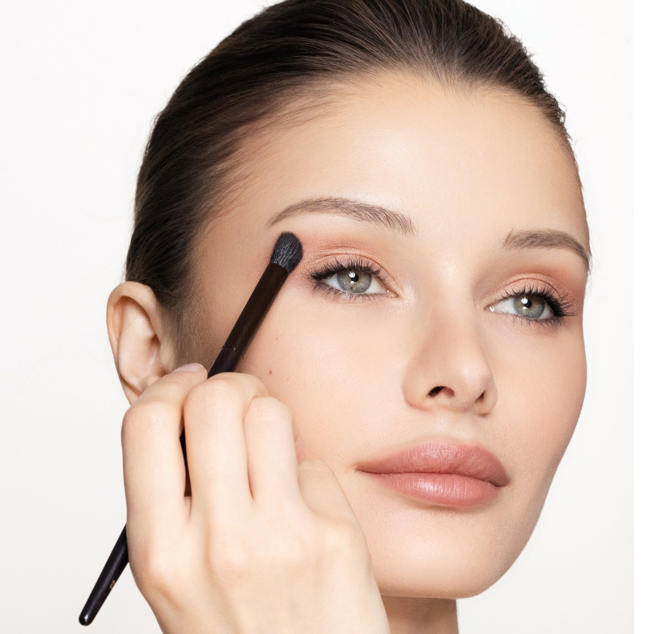 A person applying makeup with Brush 23 Place + Define to their eyebrow.