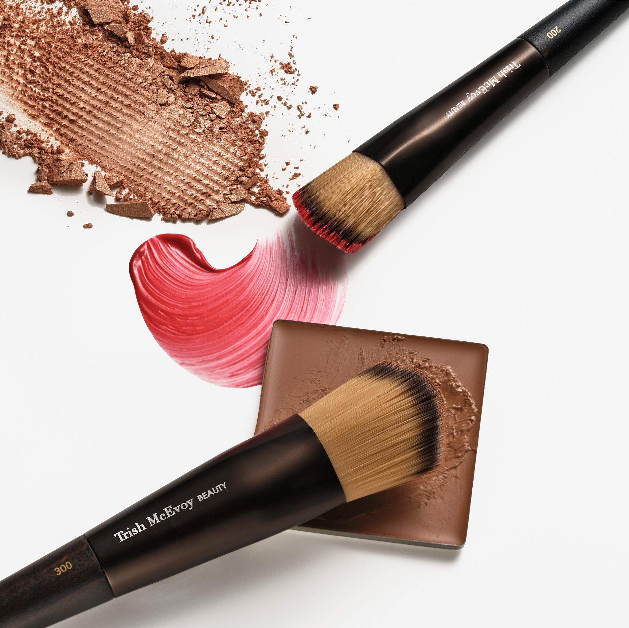 Makeup brushes with brown powder and pink cream on a white background