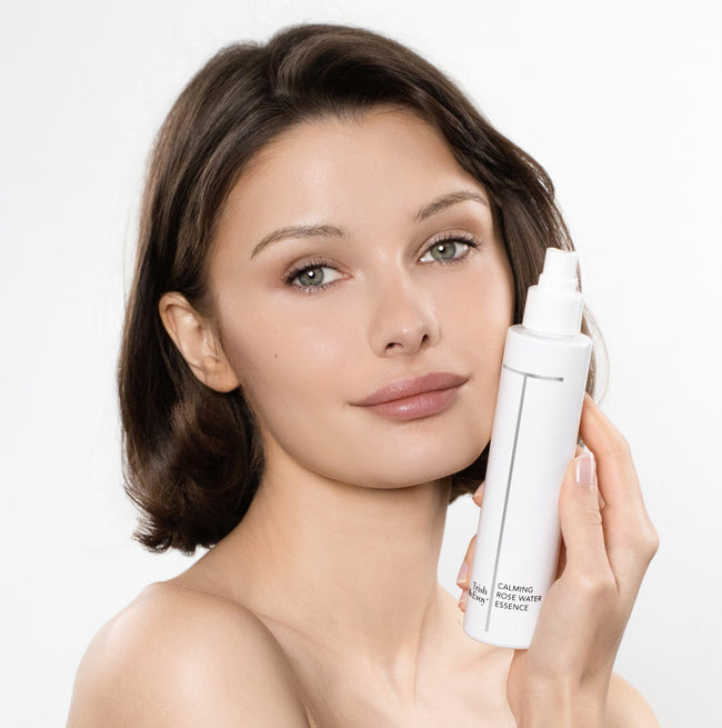 Woman holding a white skincare bottle against a white background