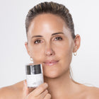 Woman holding a skincare product against a plain background