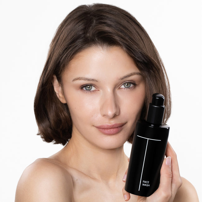 Woman holding a black skincare bottle with a white label on a white background