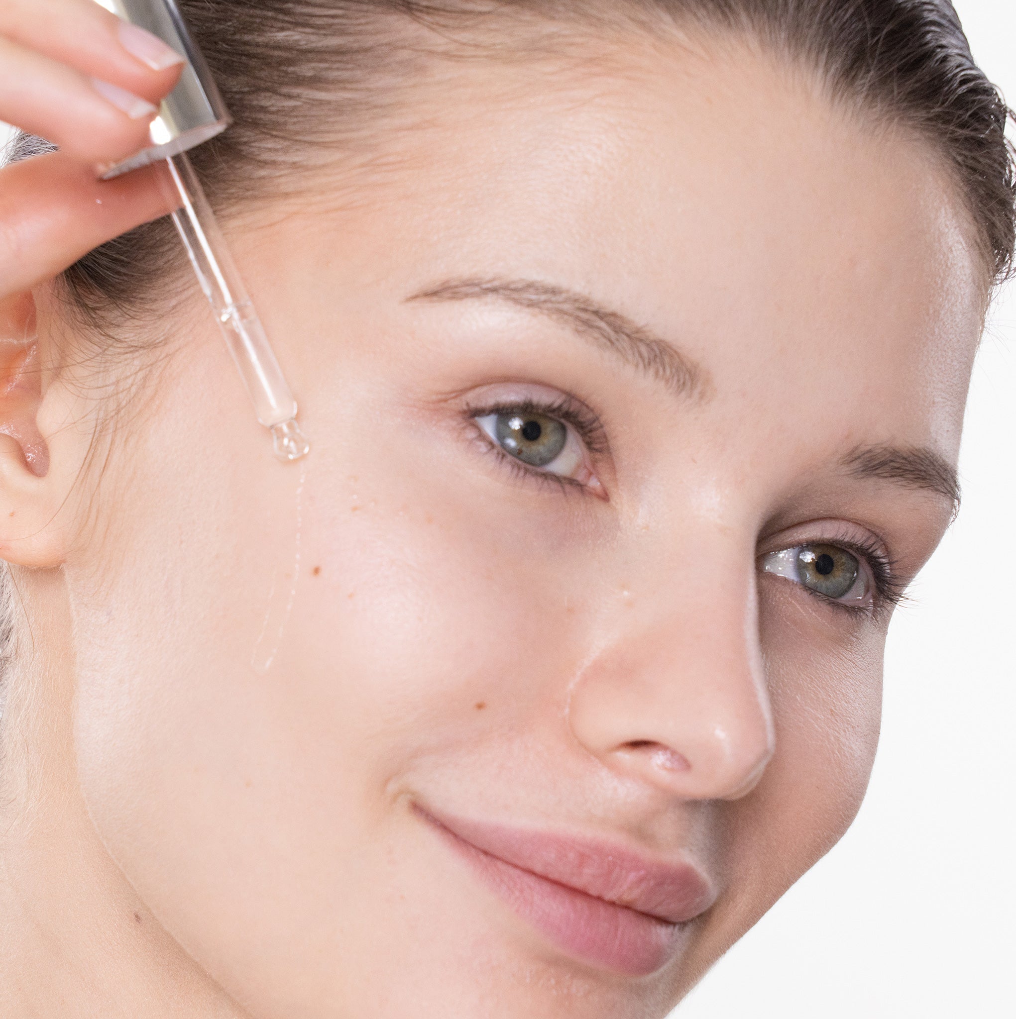 Close-up of a woman applying a face serum to her face against a white background
