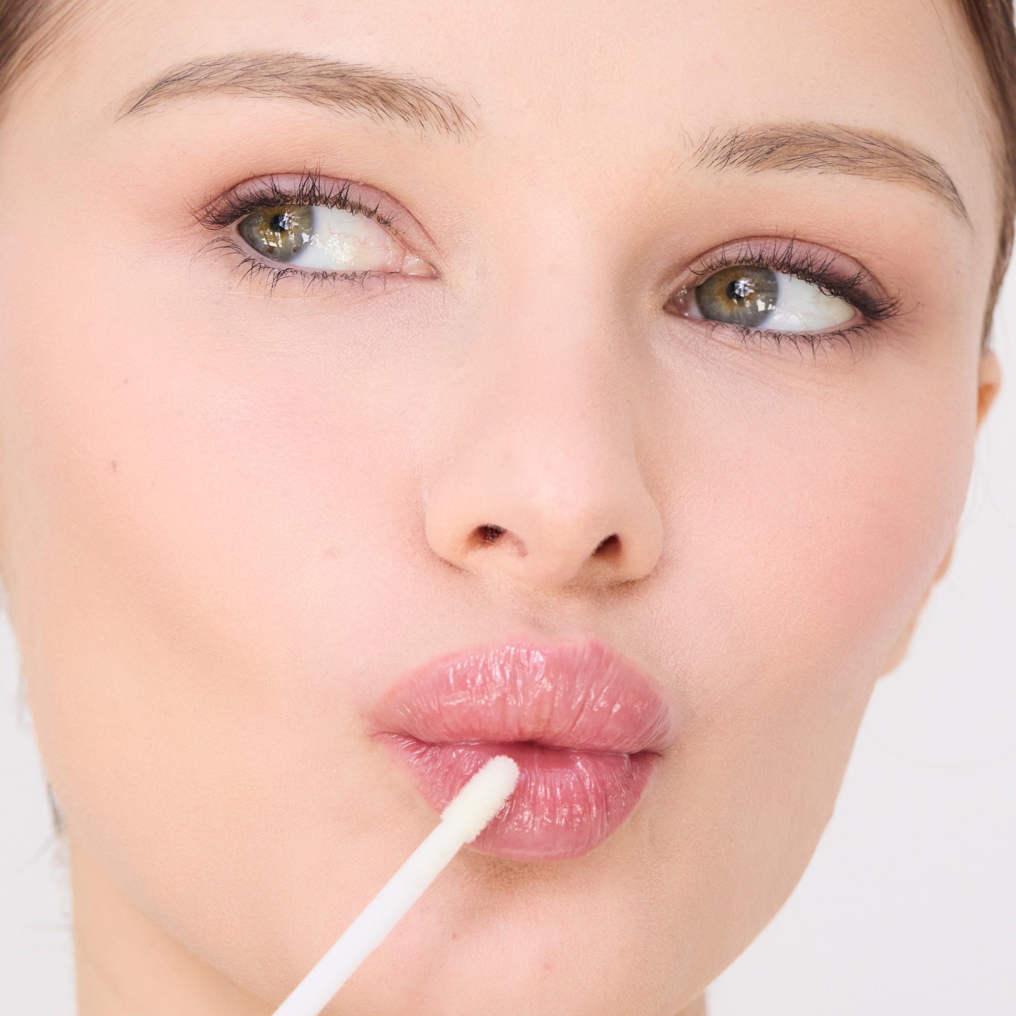 Close-up of a woman applying lip balm with a white applicator on a light background