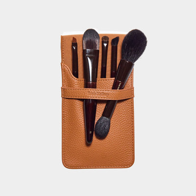 Set of makeup brushes in a brown leather holder on a light gray background