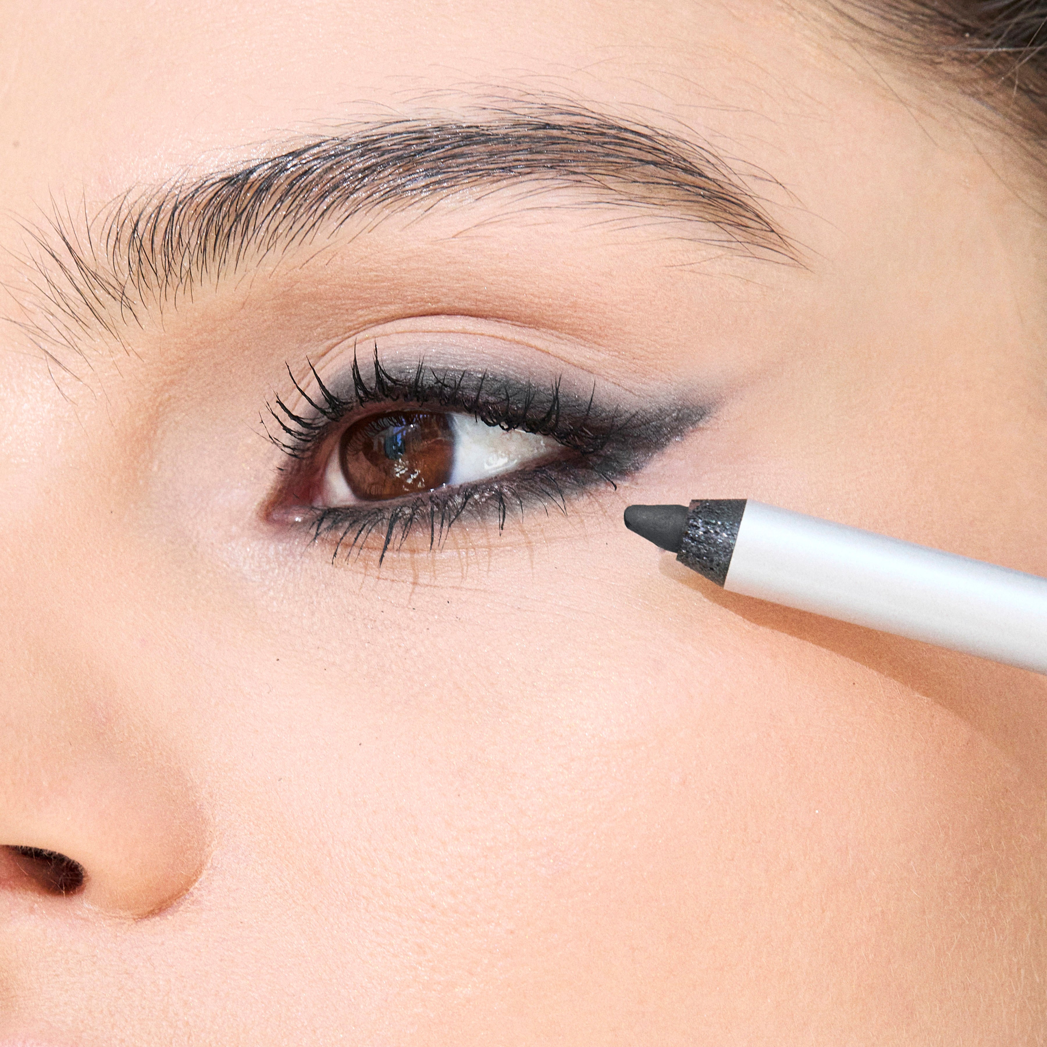 Black gel eyeliner pencil with white barrel applied to upper eyelid in winged liner style.