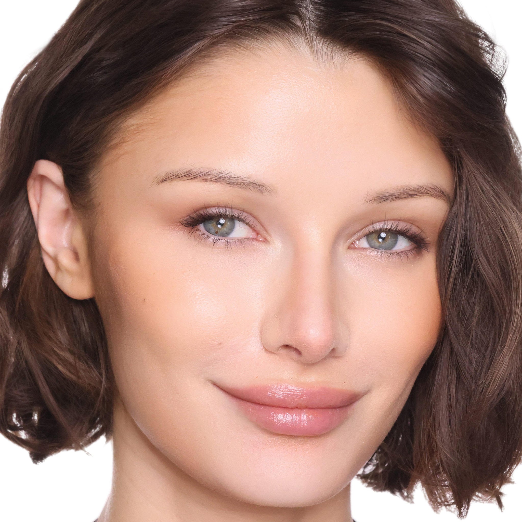 A close-up portrait of a woman with short brown hair, wearing a glossy, matte nude pink lip color and natural makeup against a solid white background.
