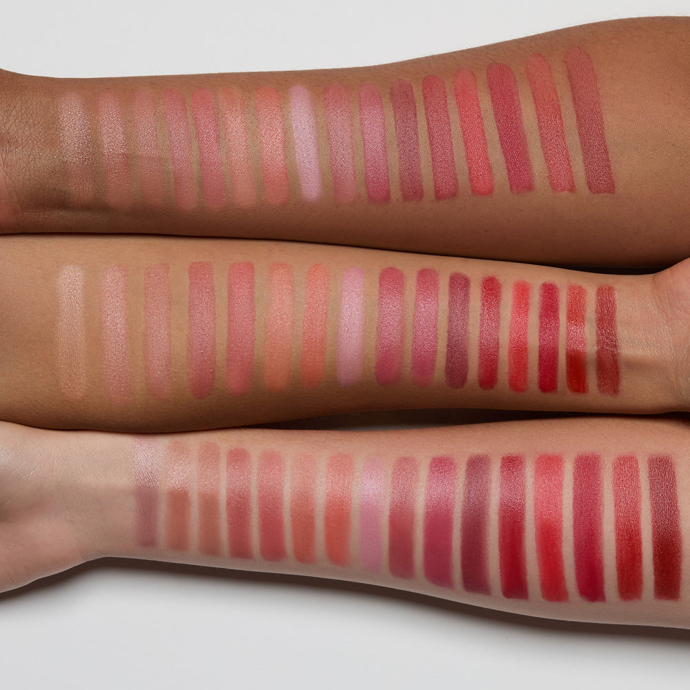 Multiple rows of lip swatches on a person's arm with various shades of pink, red, and brown.
