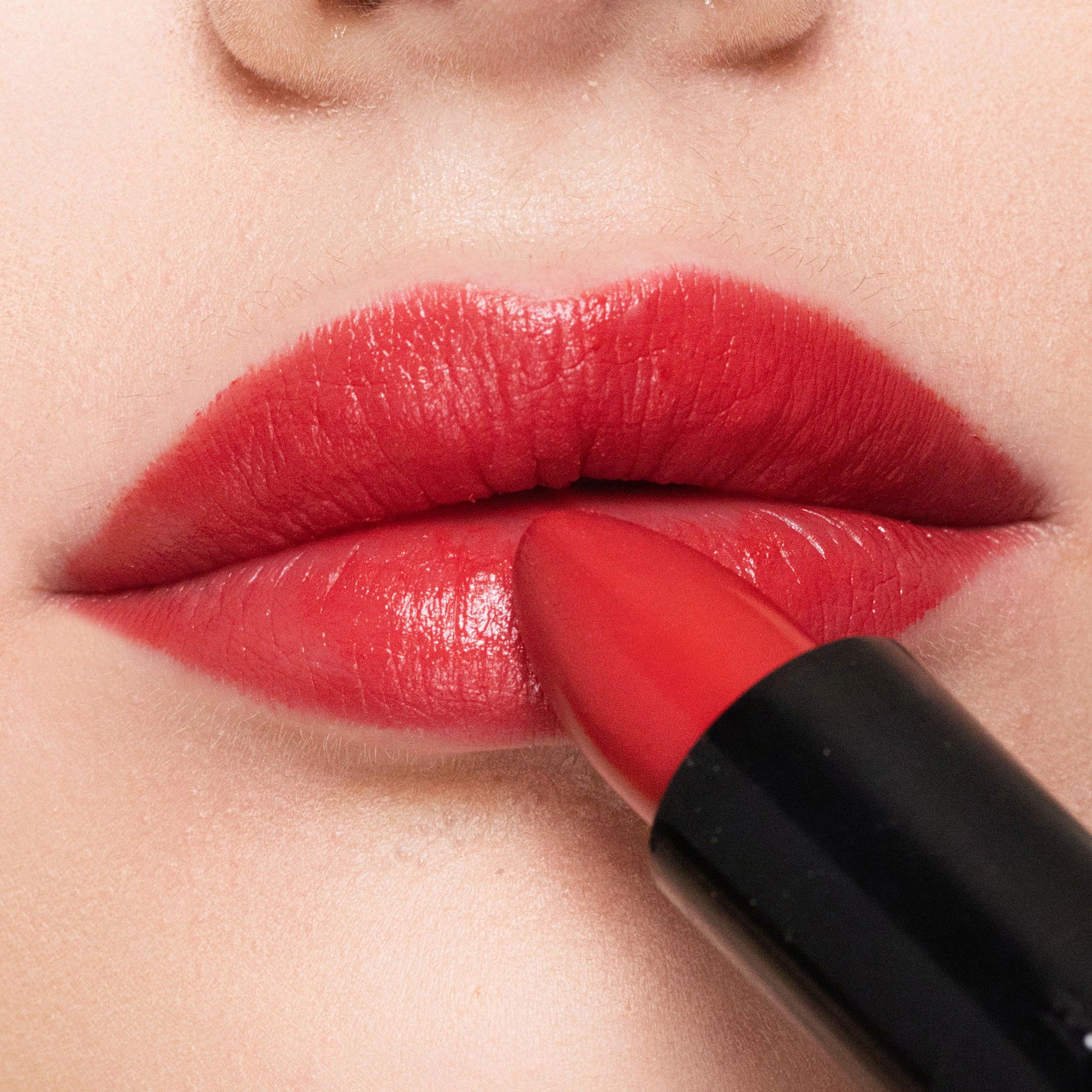 Close-up of a person applying color rendezvous lipstick to their lips.