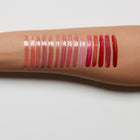 Row of lip gloss swatches on a person's arm with a light gray background