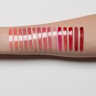 Row of lip gloss swatches on a person's arm with a light gray background