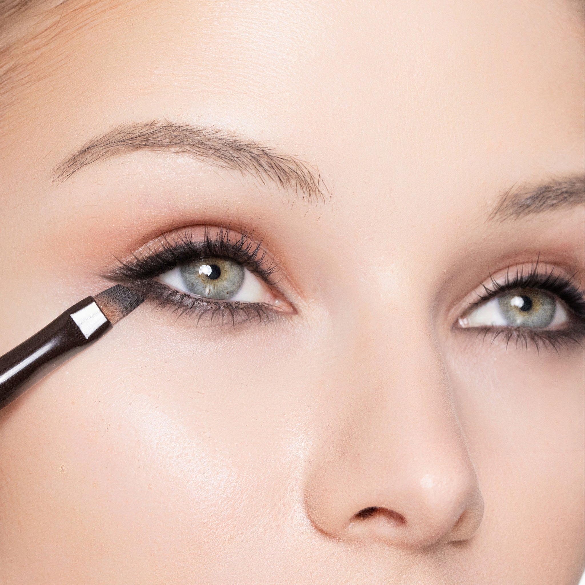 Close-up of a person applying color black eye definer with a brush.