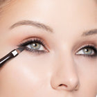Close-up of a person applying color black eye definer with a brush.