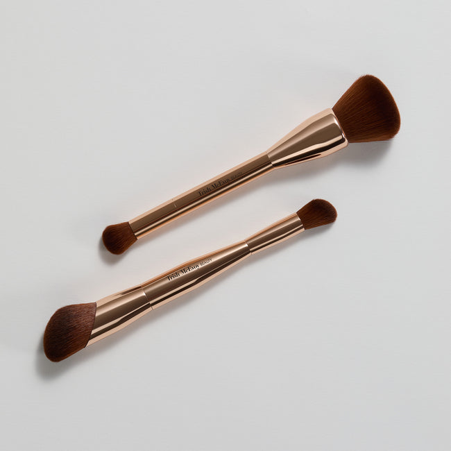 Two makeup brushes with rose gold handles on a light gray background