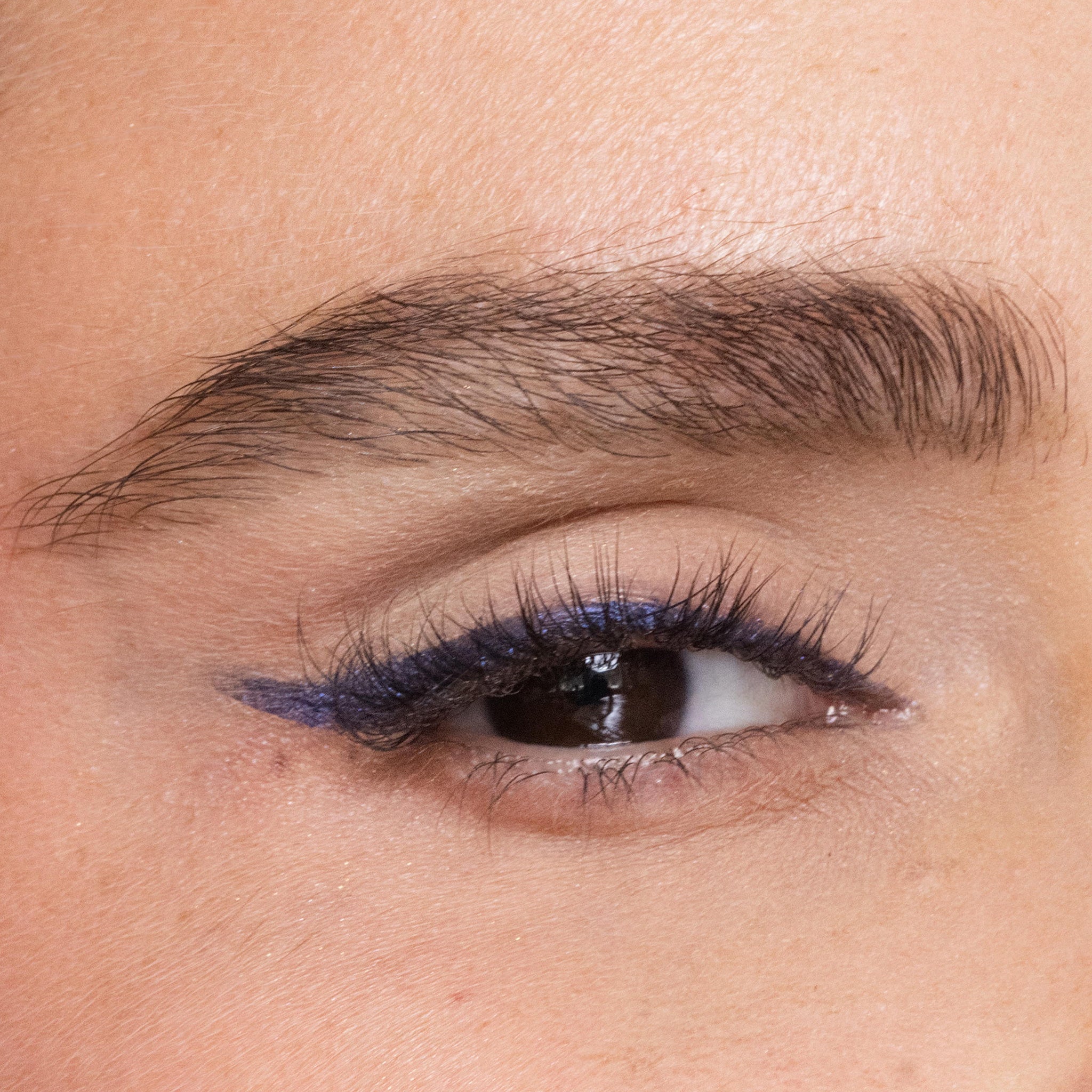 Close-up of a woman's eye with color arabian nights eyeliner on a beige background