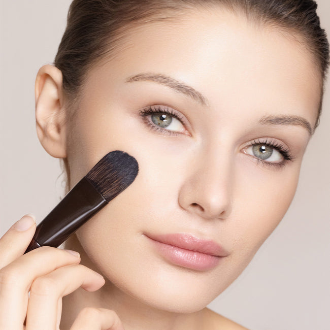 Woman applying makeup with a brush on a neutral background