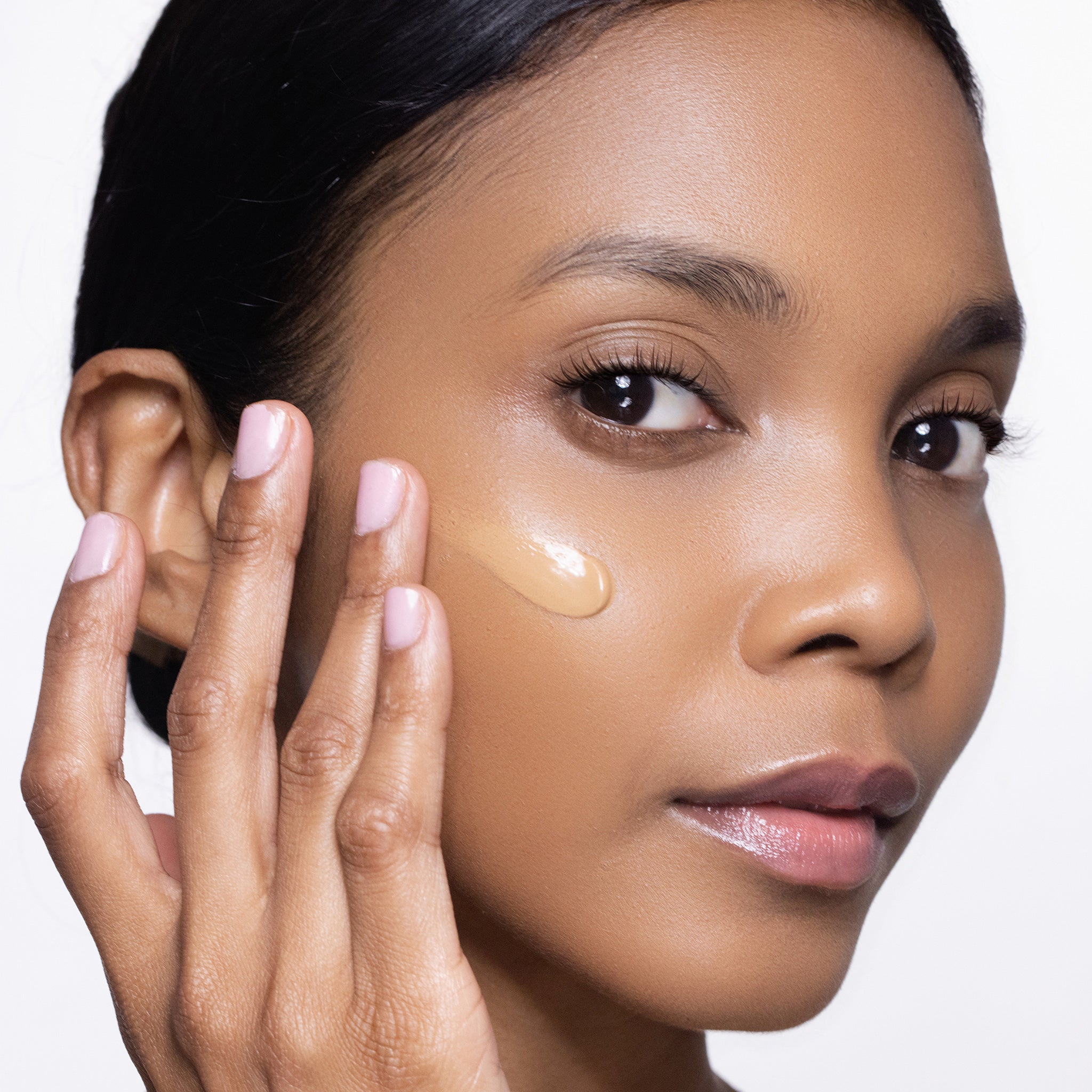 Woman applying a cosmetic product to her face with a neutral background