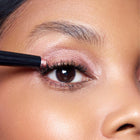 Close-up of a person applying color Bliss makeup to their eye with a brush.