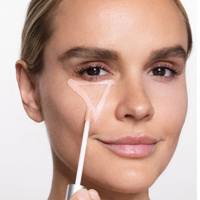 Woman applying skincare product with a brush on a neutral background