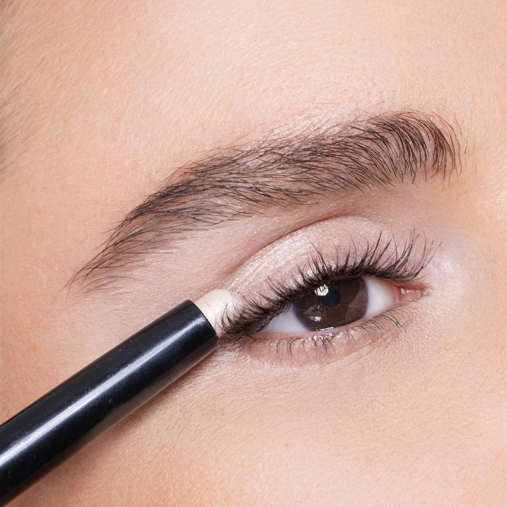 Close-up of an eye applying color white peach eyeliner.