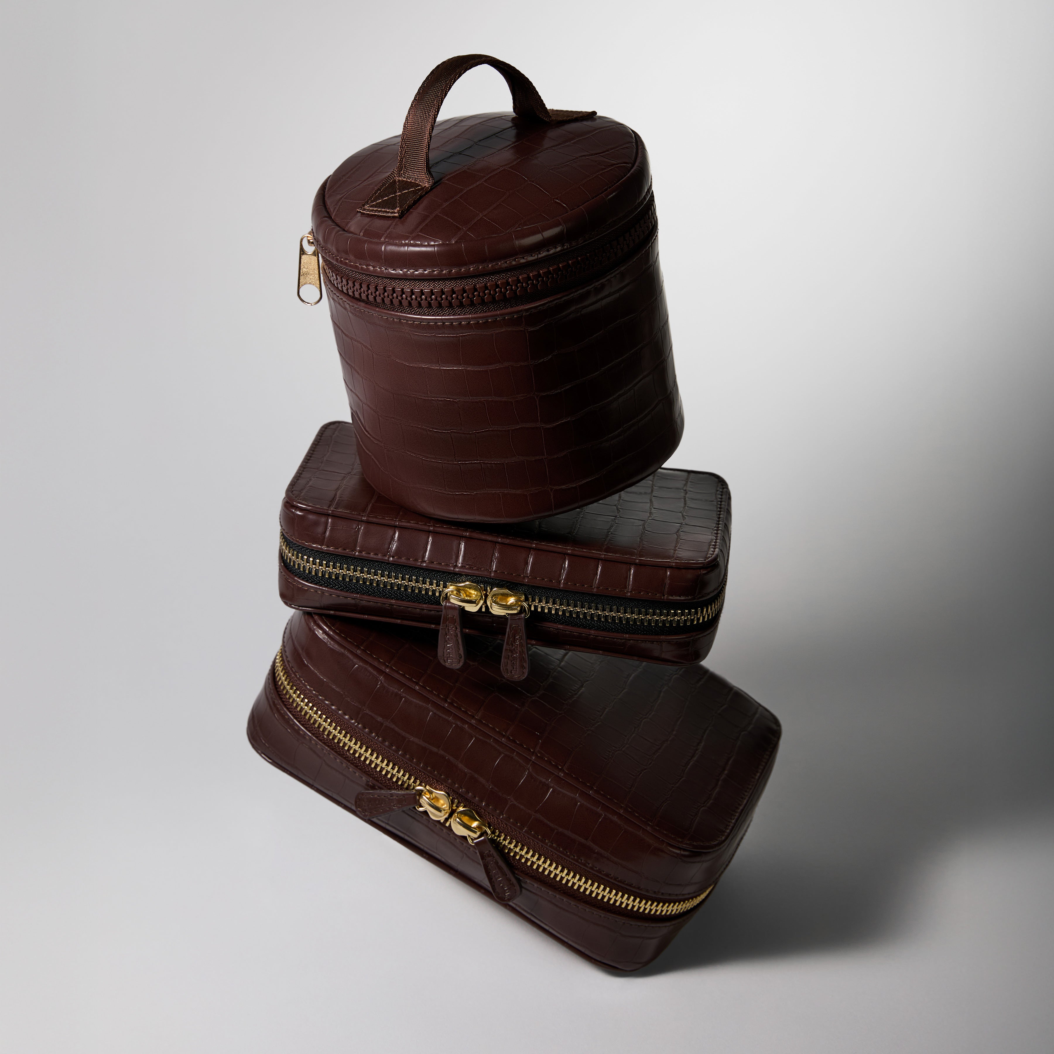 Stack of brown leather cosmetic bags with gold zippers on a gray background