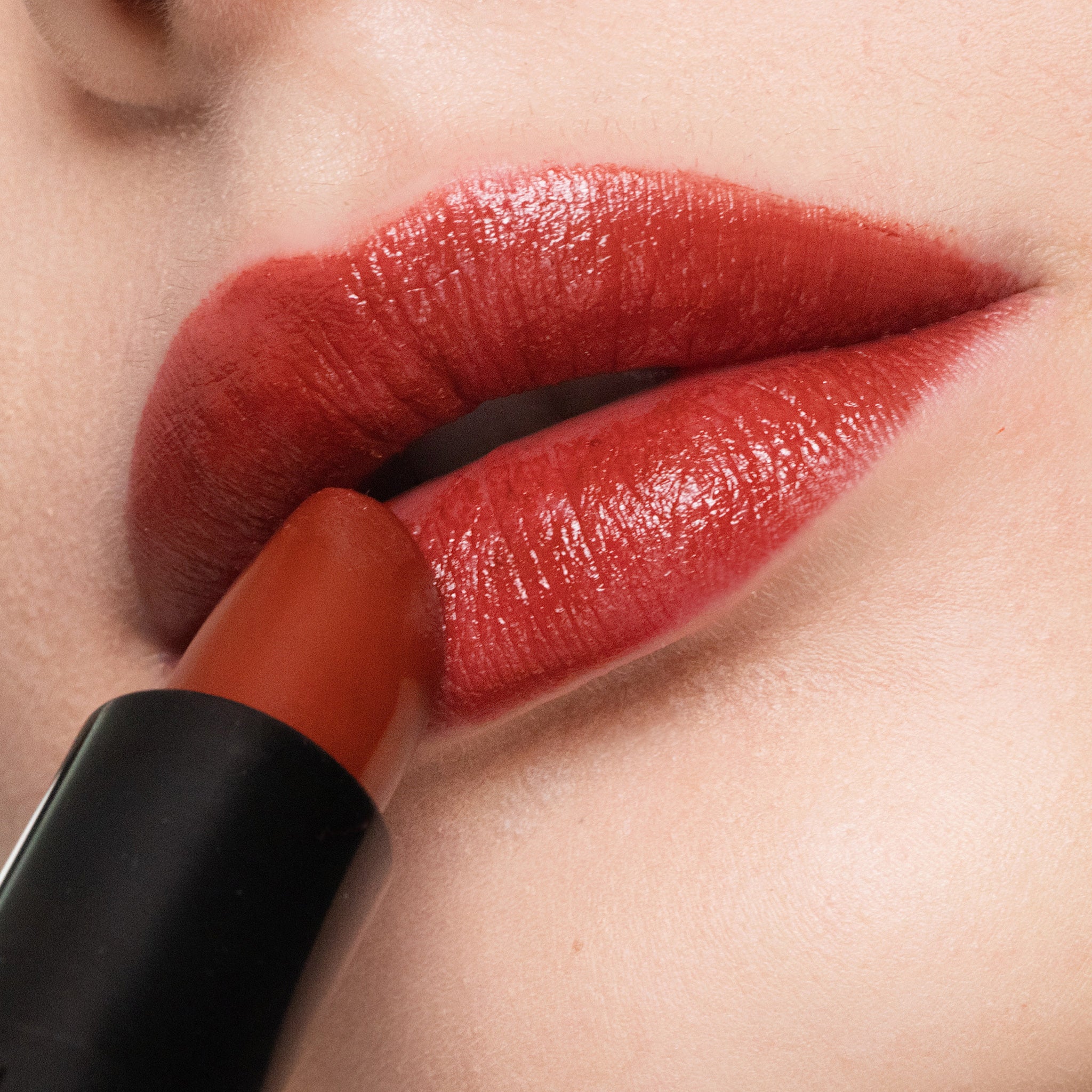 Close-up of a person applying color bordeaux lipstick to their lips.