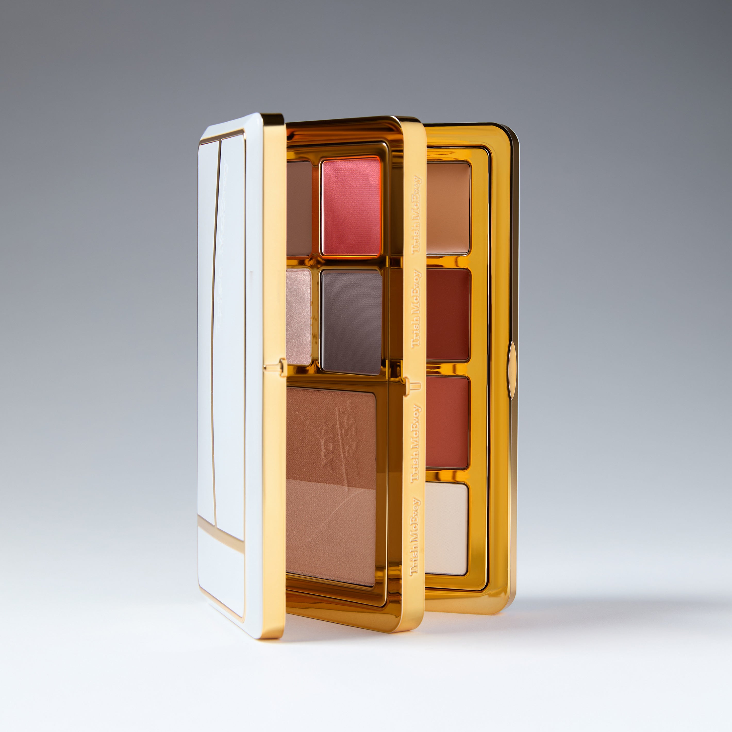 Makeup palette with multiple shades in a gold and white case on a gray background