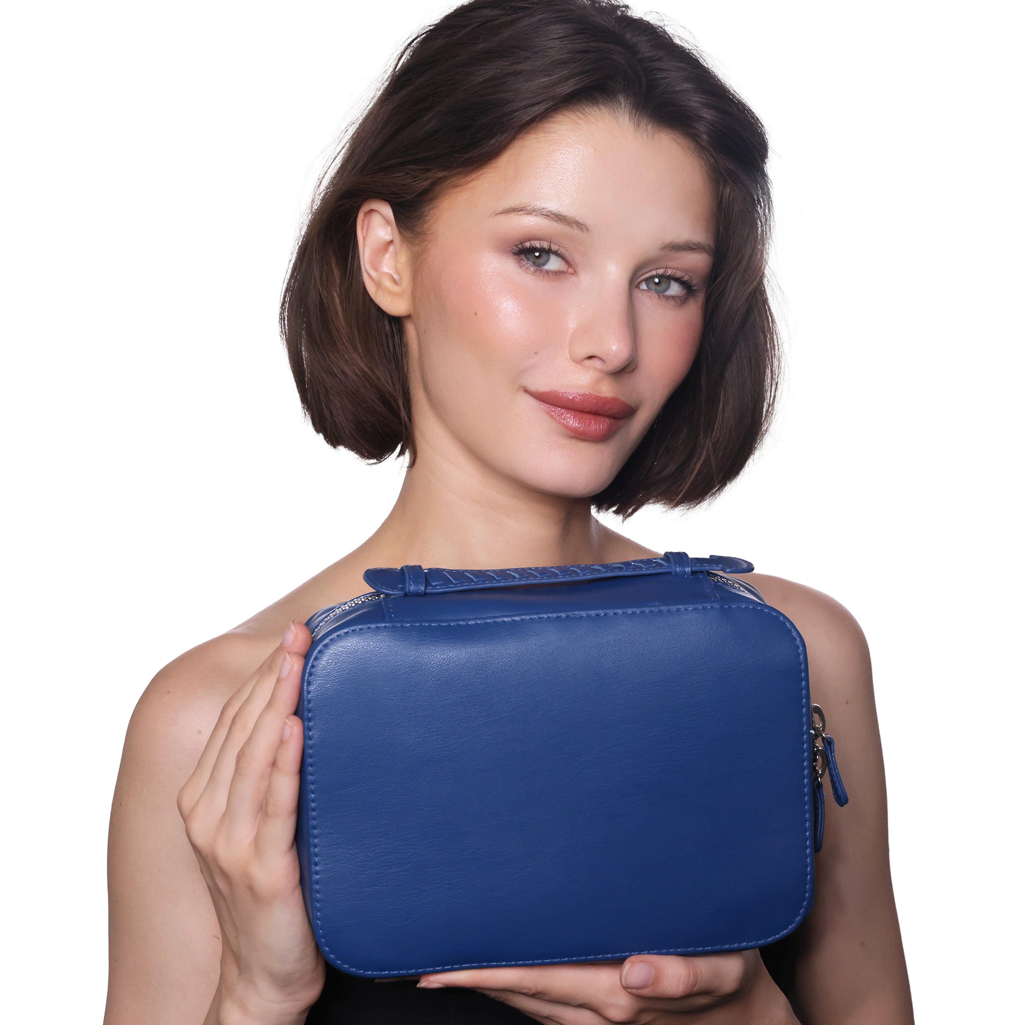 A woman with short brown hair holds a blue leather cosmetic bag against a solid white background.