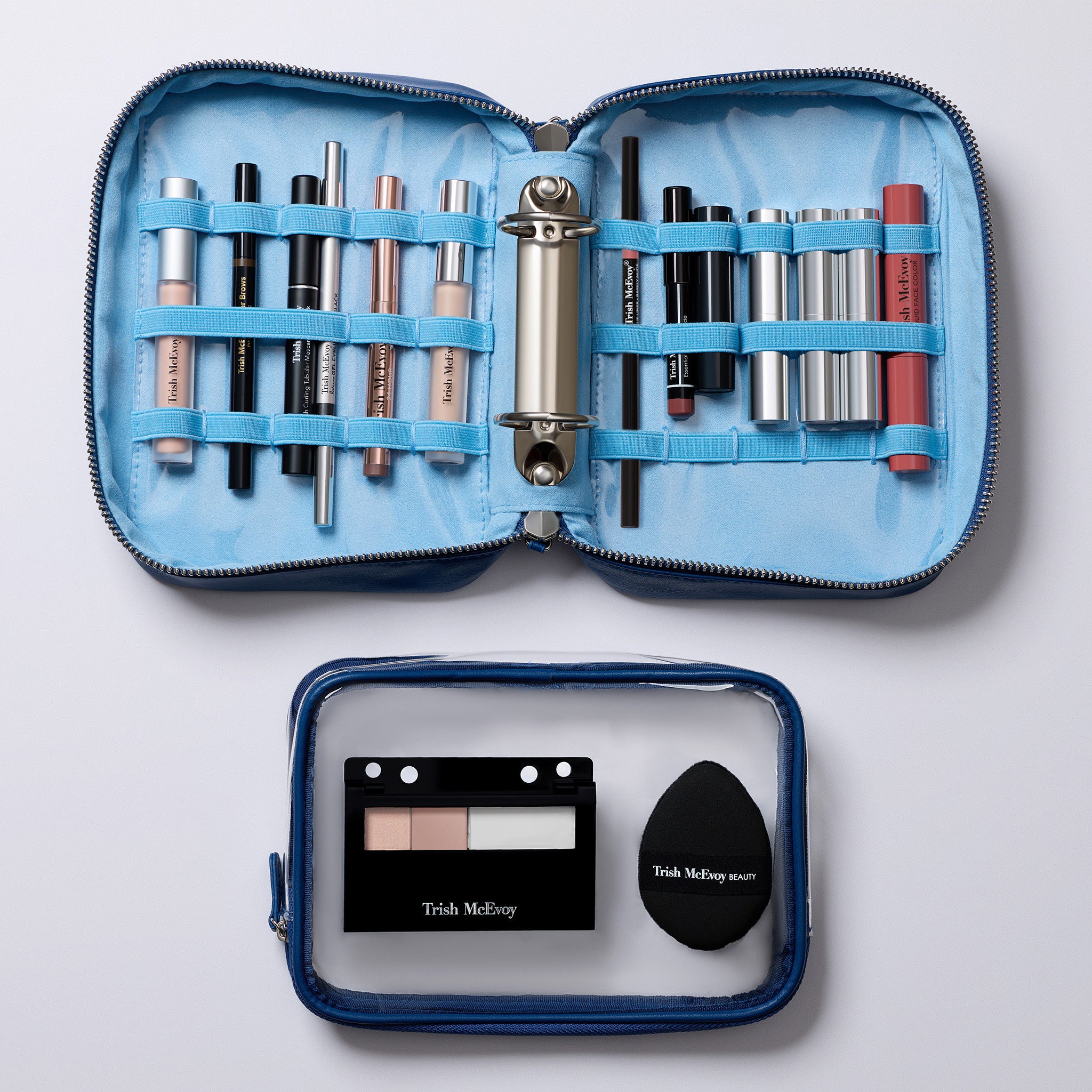 An open blue makeup organizer case with elastic loops holding multiple cosmetic items, shown above a smaller clear-and-blue Trish McElroy makeup bag containing a compact and sponge. The products are arranged on a light gray background.