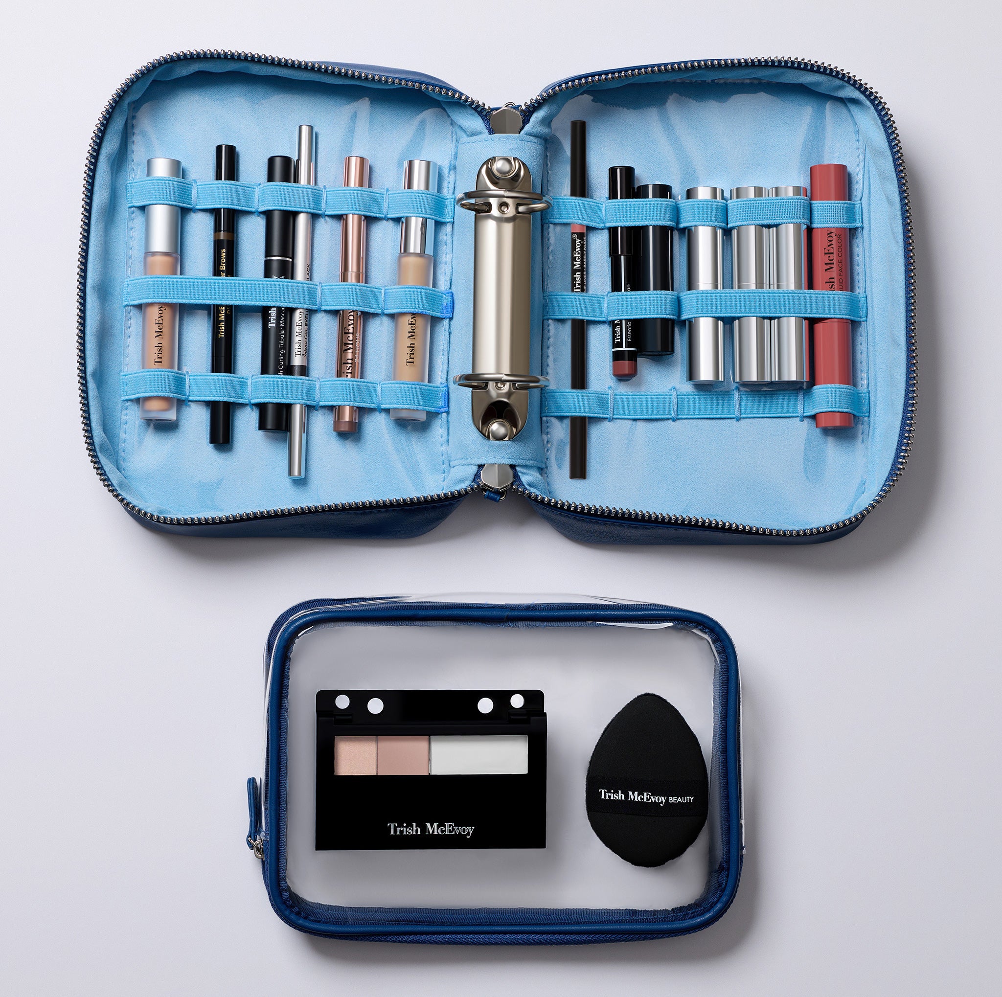 An open blue makeup organizer case on a white background, filled with cosmetics including lipsticks, pencils, and a compact. A smaller clear zip pouch with a black makeup sponge and a small makeup palette sits below it.