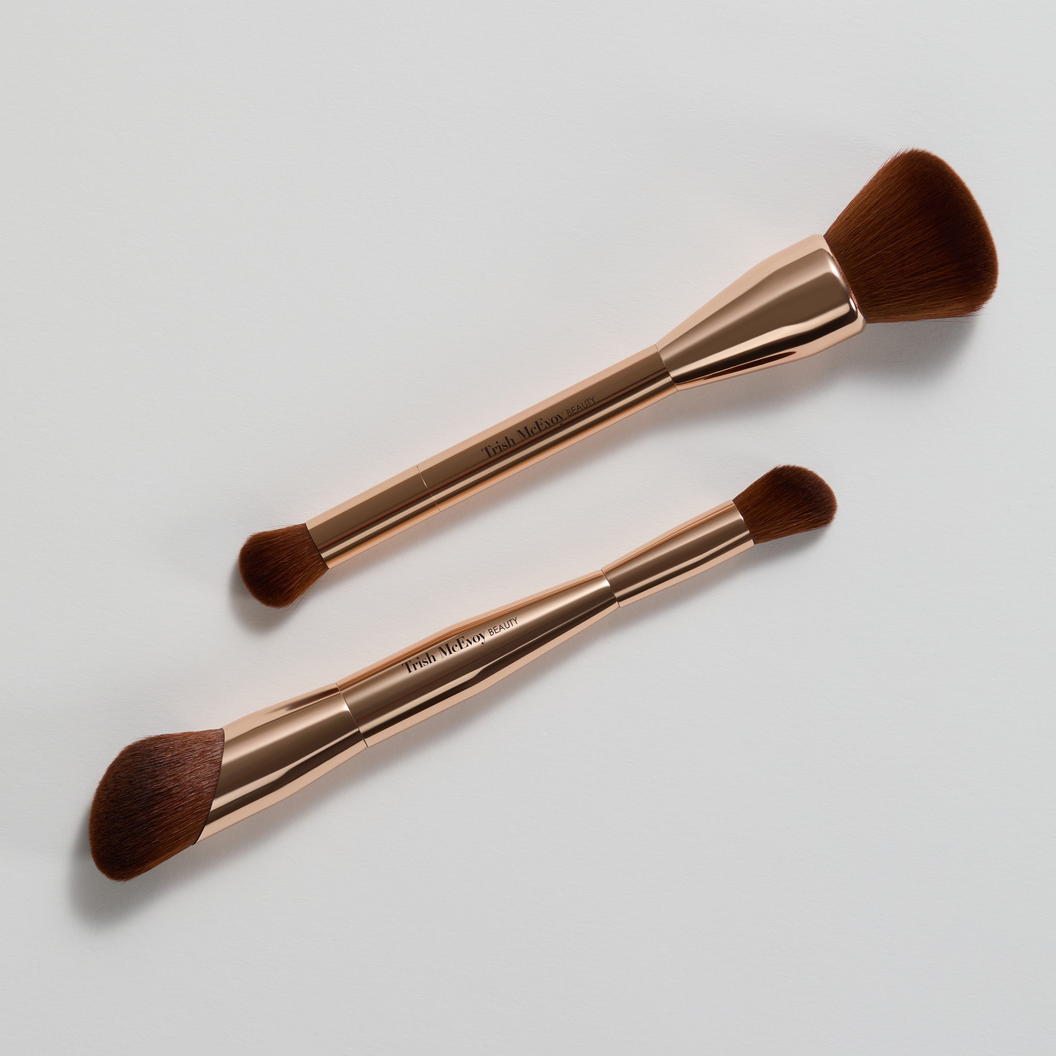 Two makeup brushes with rose gold handles on a light gray background