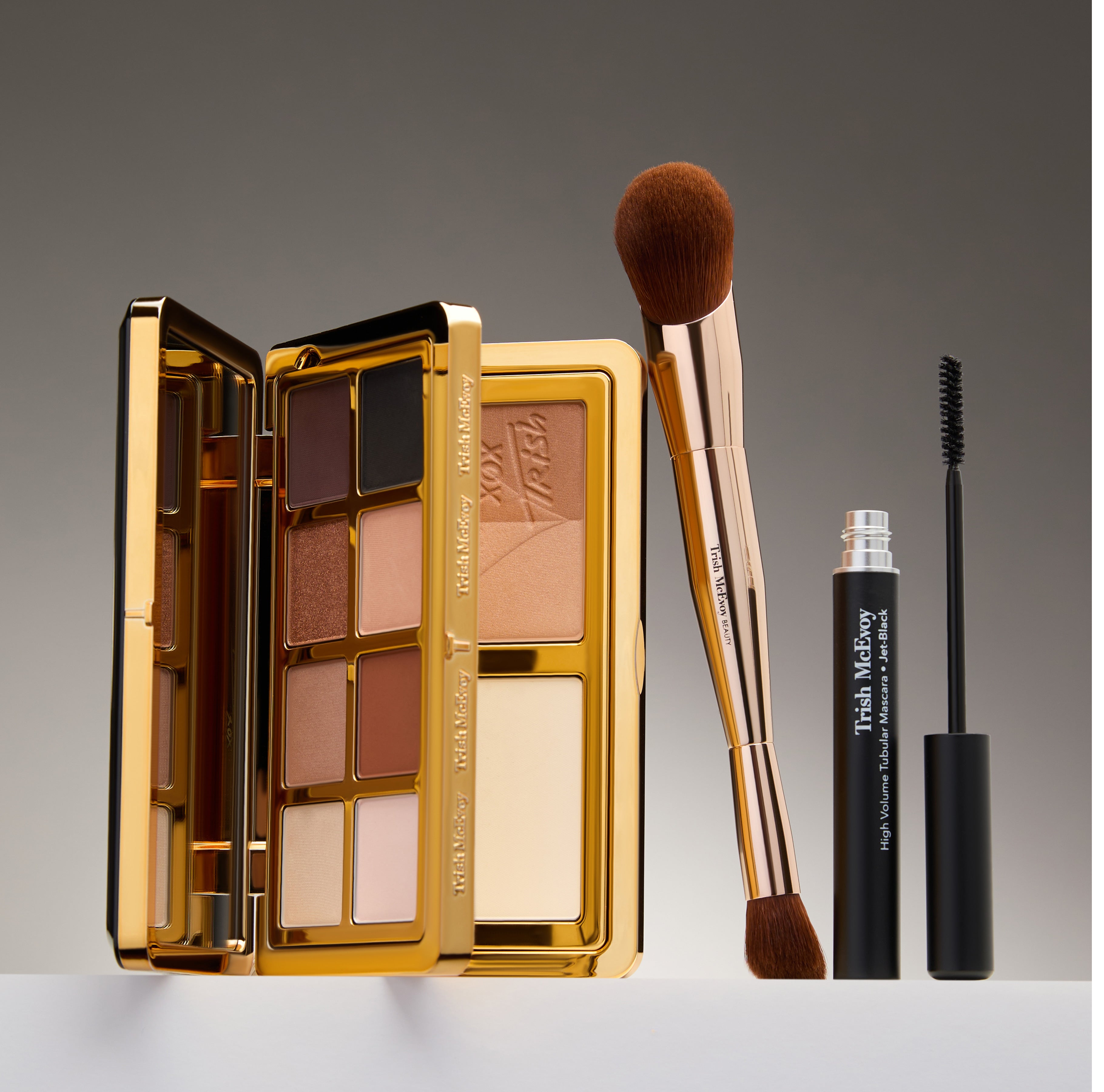 Makeup palette, brush, and mascara on a gray background